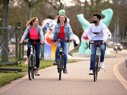 Drei junge Menschen auf Fahrrädern in Hannover  - im Hintergrund sind die Nana Skulpturen zu erkennen